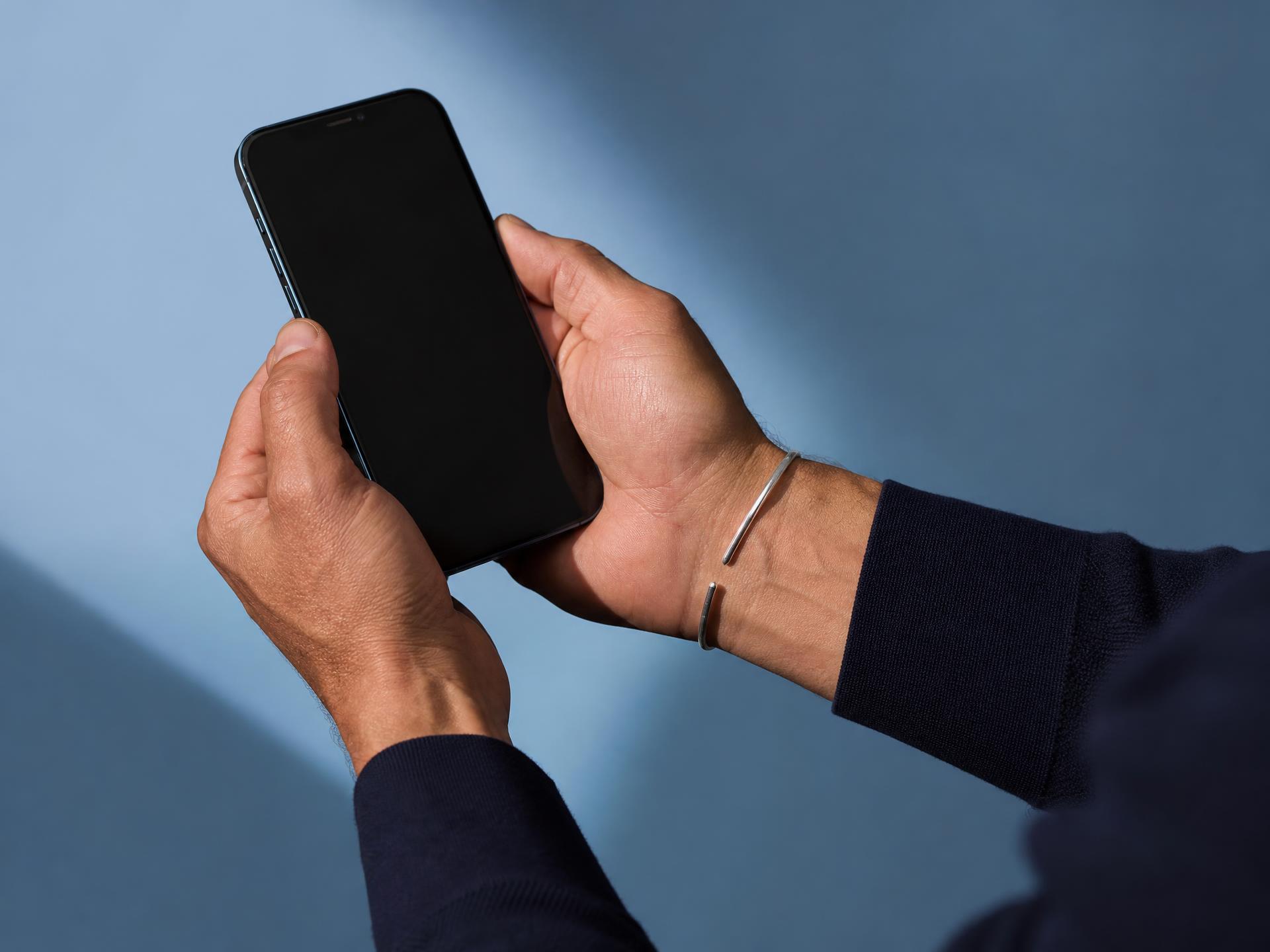 Męskie dłonie z cienką srebrną bransoletką trzymające telefon — zmiana treści sklepu rozmową z AI
